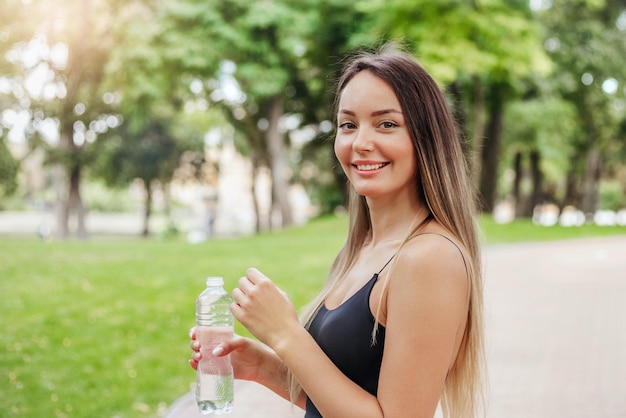 Garota feliz e sorridente foi correr no parque com uma garrafa de água Esportes e estilo de vida saudável