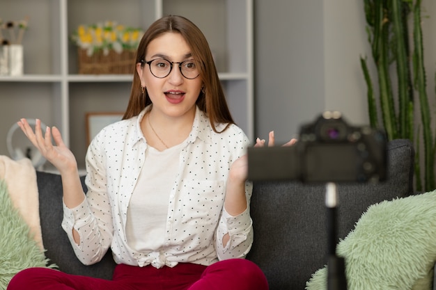 Garota feliz em casa falando na frente da câmera. Pessoas e tecnologia, jovem mulher no trabalho como vlogger. Influenciador da Web gravando mensagem para redes sociais na Internet