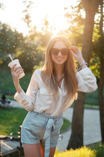 Garota feliz em óculos de sol bebendo um milk-shake e sorrindo