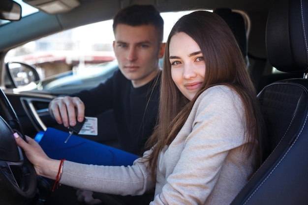 Garota feliz em um carro novo recebe uma carteira de motorista e as chaves de um jovem.