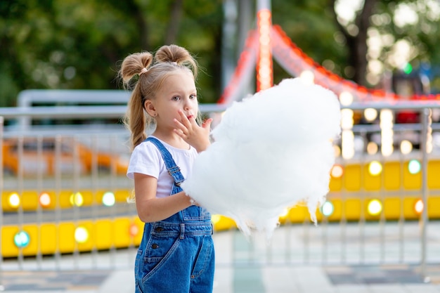 Garota feliz em um parque de diversões comendo algodão doce no verão