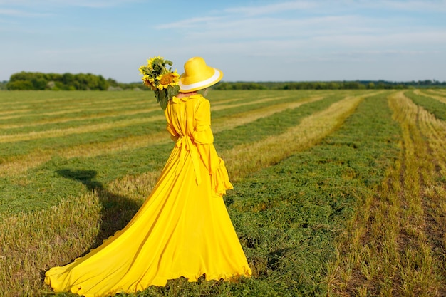 garota feliz em um vestido amarelo segura flores de girassol em um campo de girassóis contra o céu