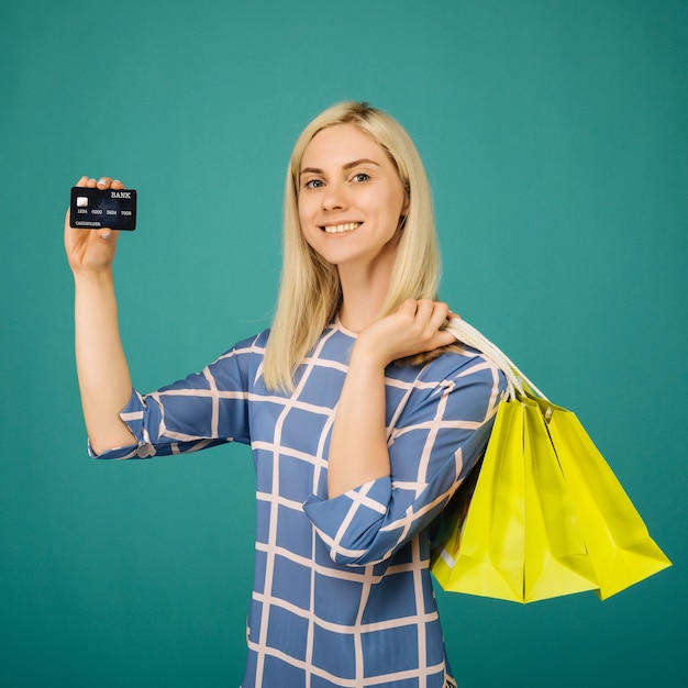 Garota feliz em uma blusa quadriculada segurando um cartão de crédito e sacolas de compras em azul