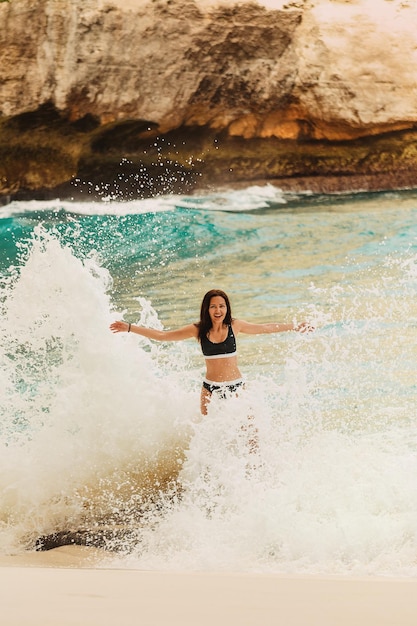 Garota feliz espirrando nas ondas. Praia de Suvehan, Nusa Penida. Indonésia