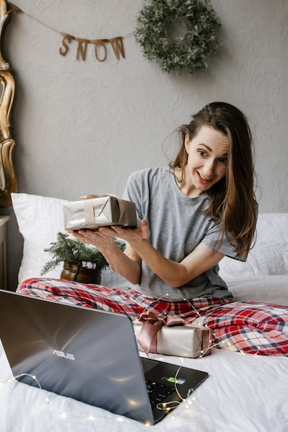 Garota feliz está sentada na frente de uma tela de computador com uma caixa de presente nas mãos em casa