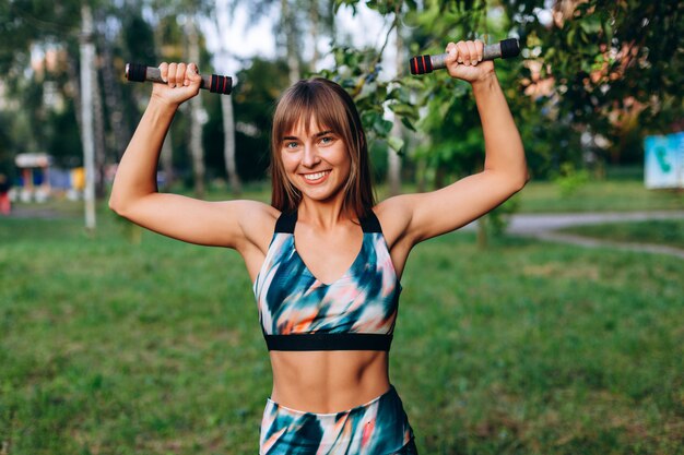 Garota feliz fazendo exercício esercise com halteres ao ar livre