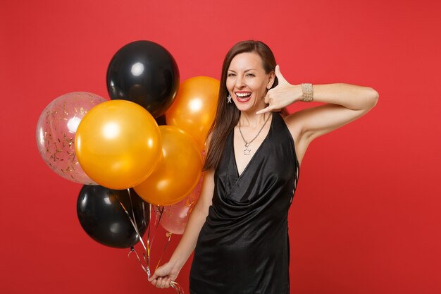 Garota feliz, fazendo o gesto do telefone, como diz, me ligue de volta com os dedos da mão, como falando no telefone, segure balões de ar celebrar isolado sobre fundo vermelho. feliz ano novo, festa de feriado de maquete de aniversário.