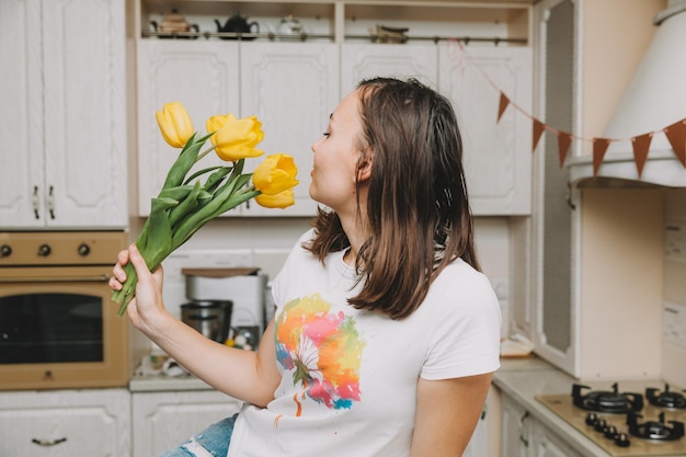 Garota feliz fica na cozinha com um buquê de flores de tulipas amarelas para o dia das mães de aniversário e páscoa