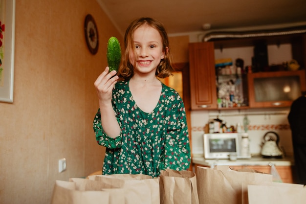 Garota feliz mostrando pepino na cozinha