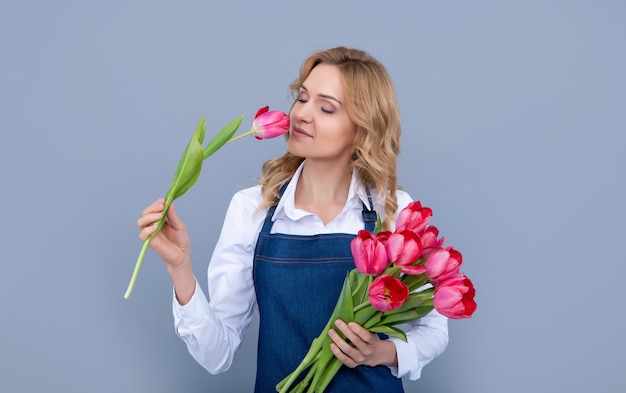 Garota feliz no avental com flores de tulipa da primavera em fundo cinza