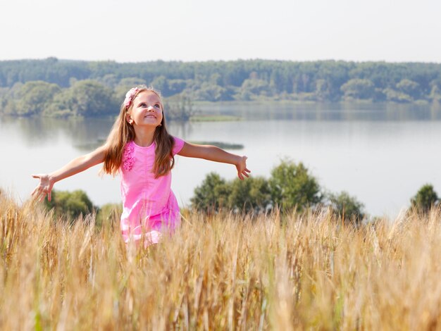 Garota feliz no campo de verão perto do lago em um dia ensolarado