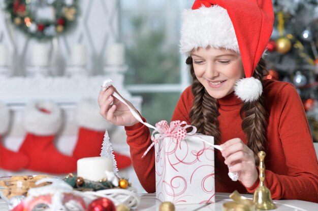 Garota feliz no chapéu de Papai Noel sentado com presente de Natal
