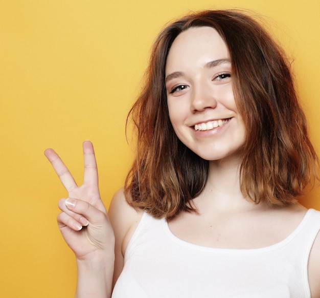 Garota feliz olhando para a câmera com sorriso e mostrando sinal de paz com os dedos