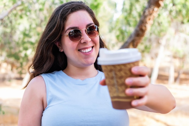 Garota feliz olhando para a câmera com uma xícara de café para viagem ao ar livre
