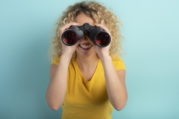 Garota feliz parece com algo binocular. Parede ciano