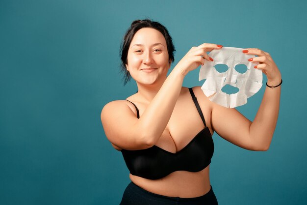 Garota feliz plus size fazendo divisão completa. Conceito positivo de corpo feliz. Eu amo meu corpo. Mulher atraente com excesso de peso com máscara hidratante branca