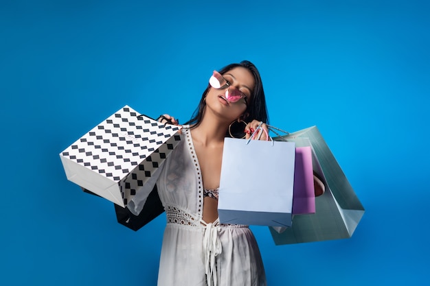 Garota feliz posando em óculos de sol gradientes com sacos de compras