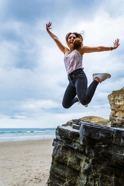 Foto garota feliz pulando na praia de areia de férias.