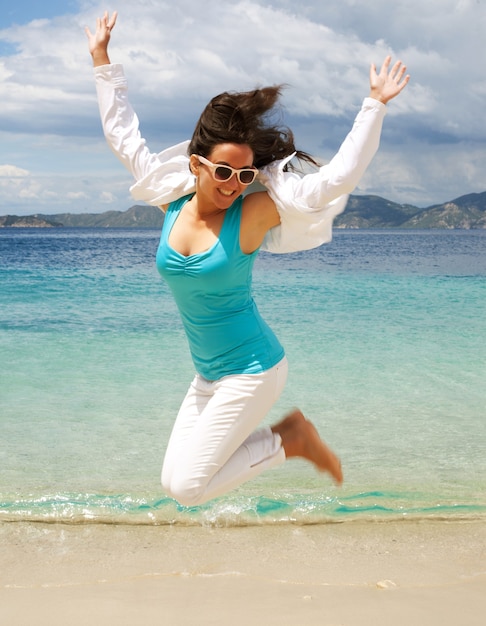 Garota feliz pulando na praia, férias de verão