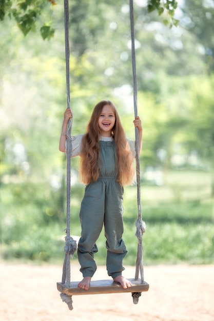 Foto garota feliz rindo com cabelo comprido, desfrutando de um passeio de balanço em um dia ensolarado de verão