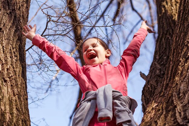 Garota feliz se divertindo na árvore Atividade de férias ativa de primavera criança escalando árvore Olá primavera