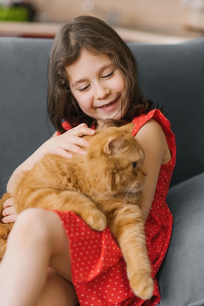 Garota feliz segura seu amado animal de estimação, um gato britânico escocês vermelho no colo e acaricia seu pelo