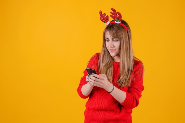 Garota feliz, segurando o smartphone nas mãos usando aro de natal engraçado