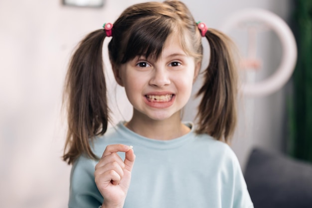 Garota feliz segurando seu dente caído na mão o retrato de uma garotinha bonitinha se alegra