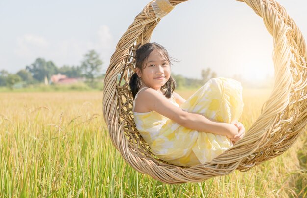 Garota feliz sentada em um balanço de vime entre campos de arroz