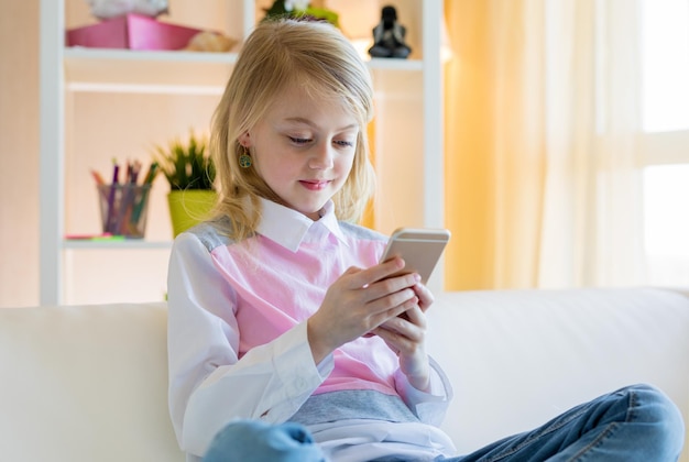 Garota feliz sentada no sofá e usando o telefone em casa