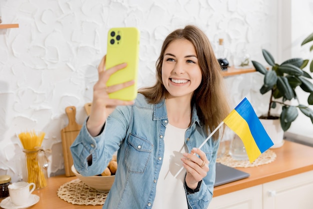 Garota feliz tira uma selfie com a bandeira da Ucrânia em sua cozinha