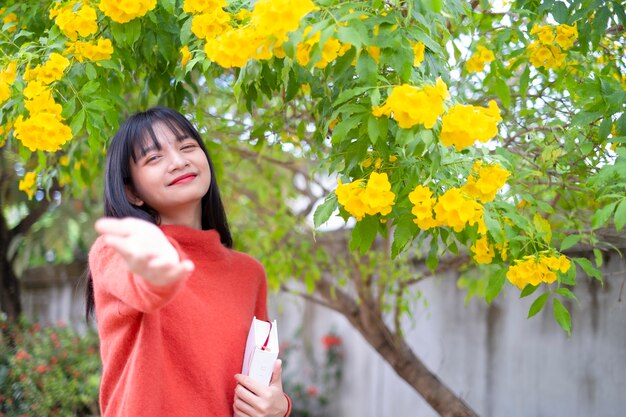 Garota feliz usar suéter laranja segurar livro sobre fundo de flor amarela.