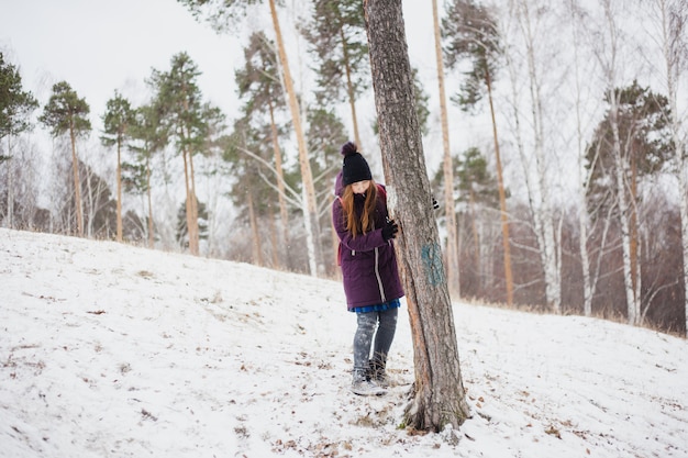 Garota fica perto de uma árvore, caminhada de inverno na floresta ou parque