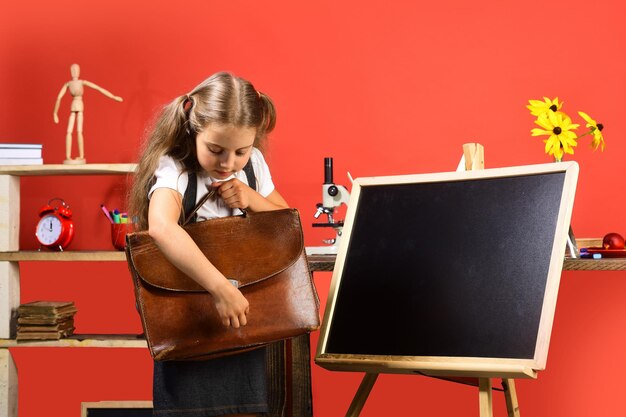 Garota fica perto do espaço de cópia do quadro-negro A estudante abre a mochila marrom