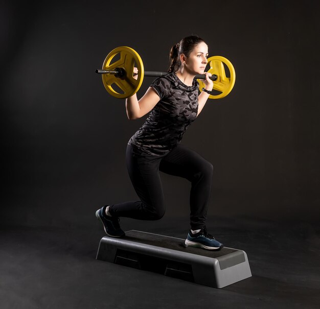 Garota fitness em uma plataforma de degraus com panquecas amarelas de barbell a puxa feliz com lindos olhos