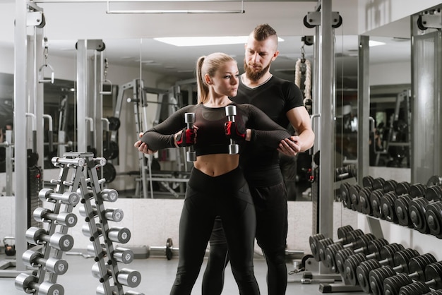 Garota fitness levantando halteres com seu treinador pessoal no ginásio