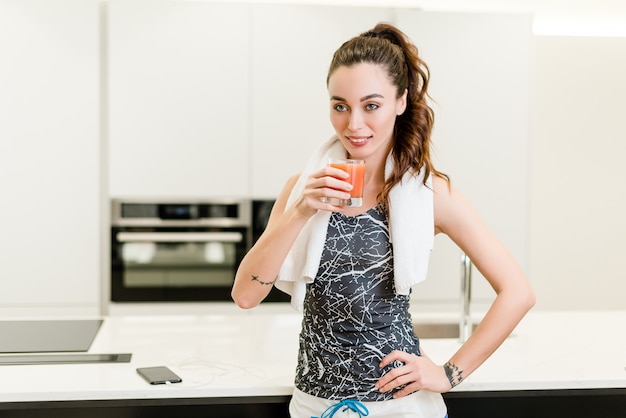 Garota fitness linda bebendo suco fresco na cozinha