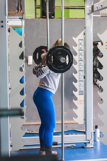 Garota fitness se preparando para fazer agachamentos com barra em uma academia