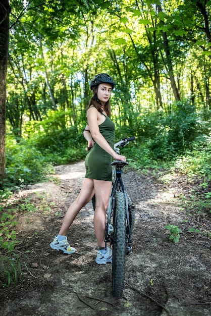 Foto garota fitness usa vestido verde anda de bicicleta de montanha moderna na floresta no dia quente de verão