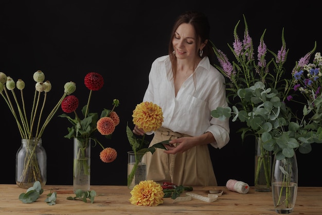 Garota florista coleta um buquê em uma oficina de flores em um layout de fundo escuro para floricultura