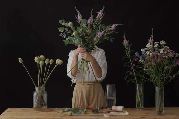 Garota florista coleta um buquê em uma oficina de flores em um layout de fundo escuro para floricultura