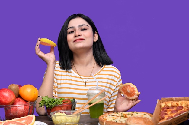 Foto garota foodie sentada à mesa de frutas sorrindo segurando frutas cítricas modelo indiano do paquistanês