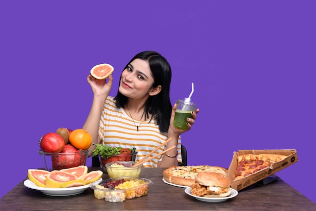 garota foodie sentada à mesa de frutas sorrindo segurando frutas cítricas modelo indiano do paquistanês