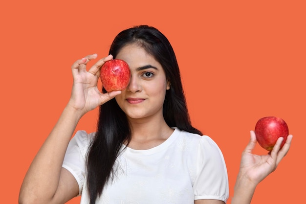 Garota foodie vestindo camiseta branca segurando uma maçã e cobrindo os olhos com um modelo indiano de maçã do paquistanês