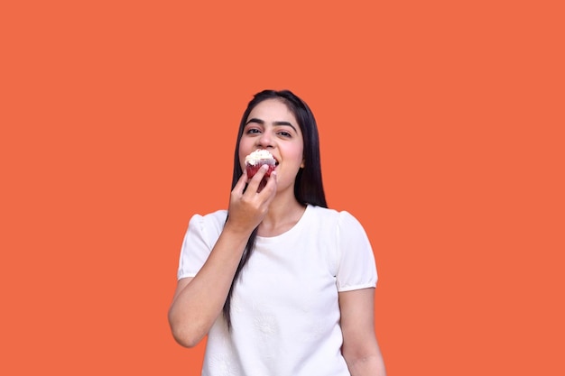 Garota foodie vestindo camiseta e comendo bolinho sobre fundo laranja modelo indiano do paquistanês