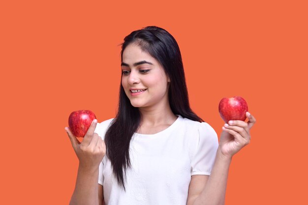 Garota foodie vestindo uma camiseta branca segurando maçãs e olhando para isso modelo indiano do paquistanês