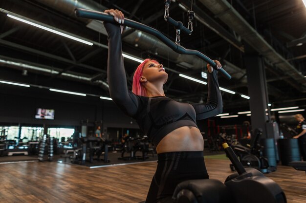 Garota forte e esportiva em um agasalho de treino preto se senta e se exercita na academia