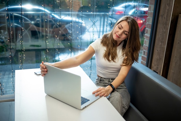 Garota freelance sorridente trabalhando em um laptop em um café dia de trabalho de uma jovem livre