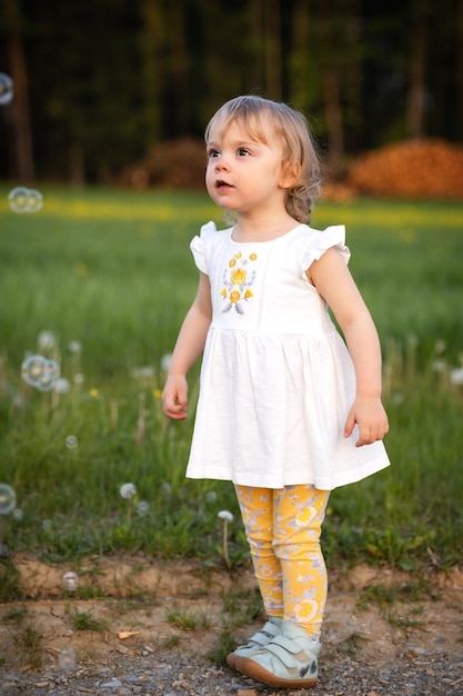 Garota gentil de vestido leve de verão em um prado olha para bolhas de sabão de surpresa