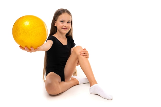 Garota ginasta sentada no chão com bola de ginástica em um fundo branco com espaço de cópia.